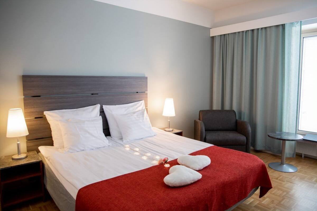 Une chambre d’hôtel avec un grand lit, deux lampes de chevet, une chaise et une petite table.