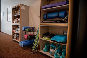 Een hal met een boekenplank vol boeken en een rek met yogamatten en kettlebells.