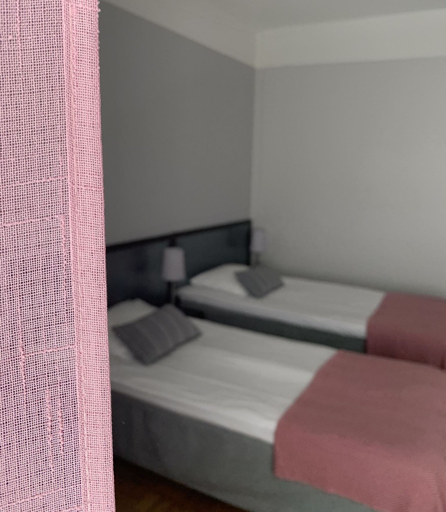 Una habitación con dos camas individuales, una mesita de noche con lámpara y una cortina rosa.