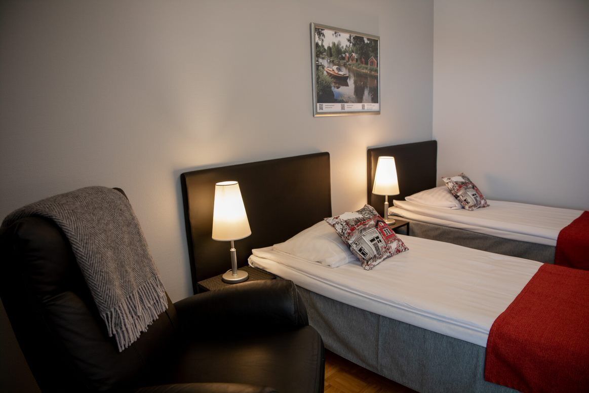 Ein Hotelzimmer mit zwei Einzelbetten, einem Sessel, einem Nachttisch mit Lampe und einem gerahmten Bild an der Wand.