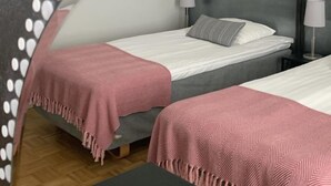Quarto de hotel com duas camas, cada uma com manta rosa e branca estampada, e um espelho redondo com pontos brancos na parede.