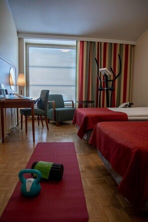 Een hotelkamer met twee bedden, een bureau met lamp, een stoel, een loopband en fitnessapparatuur.
