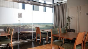 Sala de conferências com vista panorâmica pela janela, mesas e cadeiras de madeira e um vaso de plantas.