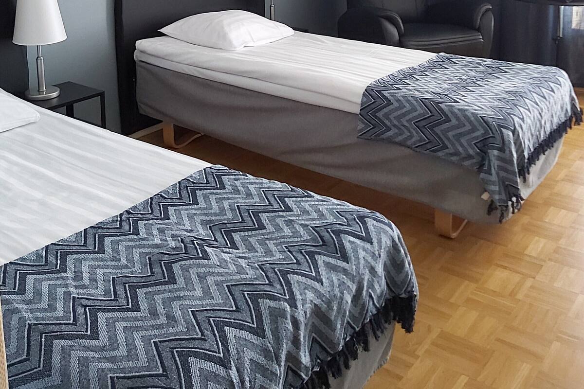 Une chambre d’hôtel avec deux lits simples, une chaise, un bureau et une lampe.