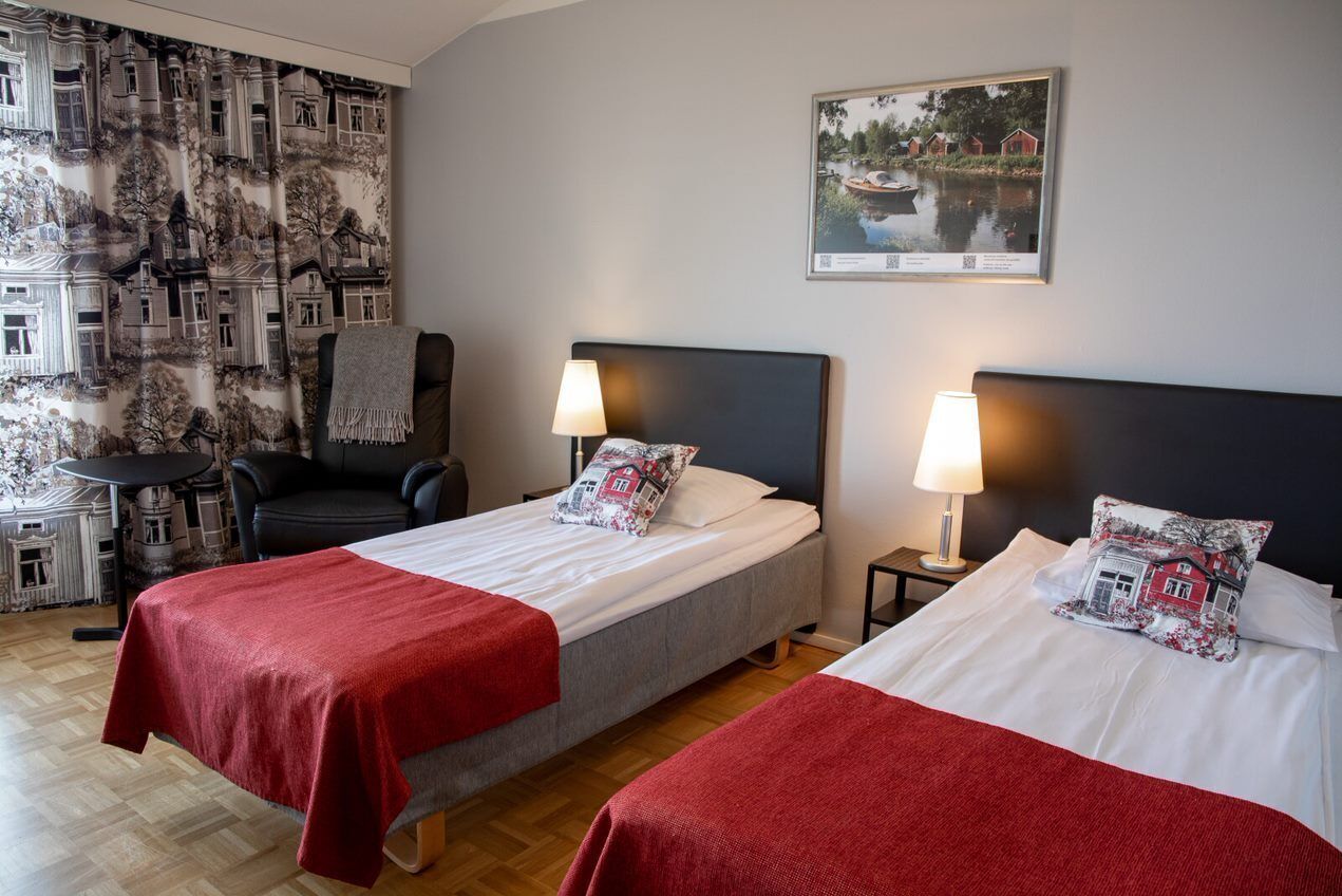 Habitación de hotel con dos camas, una silla, una mesa y una pared con una imagen impresa.