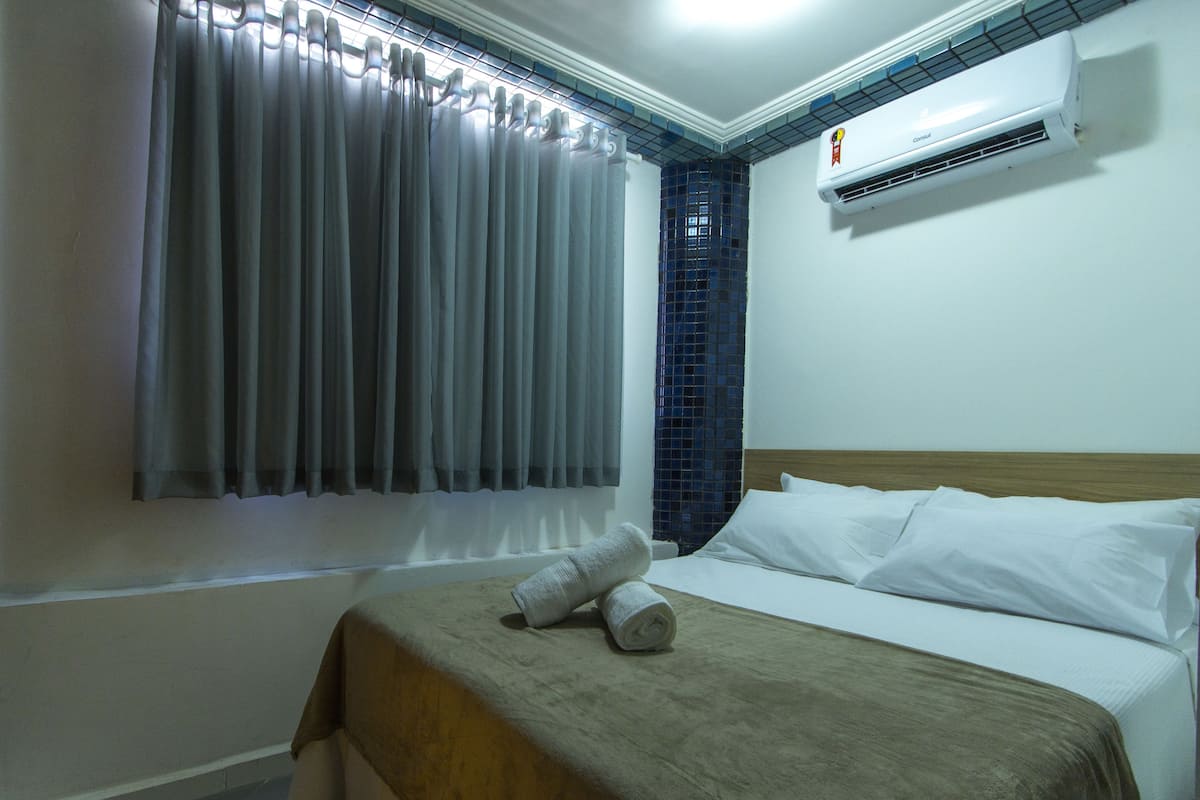 Habitación de hotel con cama, ventana con cortinas, aire acondicionado y pared de azulejos.
