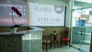 A reception area with a reception desk, a potted orchid, two chairs, and a glass door leading outside. - Hotel Sabor e Fé (Aparecida)