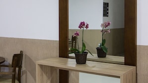 A wooden desk with a mirror, two potted orchids, and a chair in a room with white walls and a tiled floor. - Hotel Sabor e Fé (Aparecida)