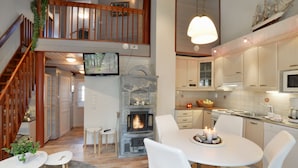 Una cocina moderna con chimenea de piedra, zona de comedor blanca y una escalera que sube a un nivel superior.