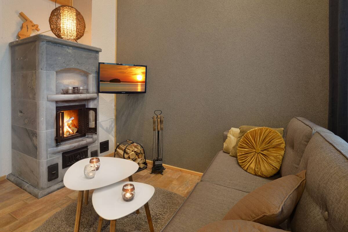Una sala de estar con chimenea de piedra, televisor montado en la pared, sofá y una mesita con velas.