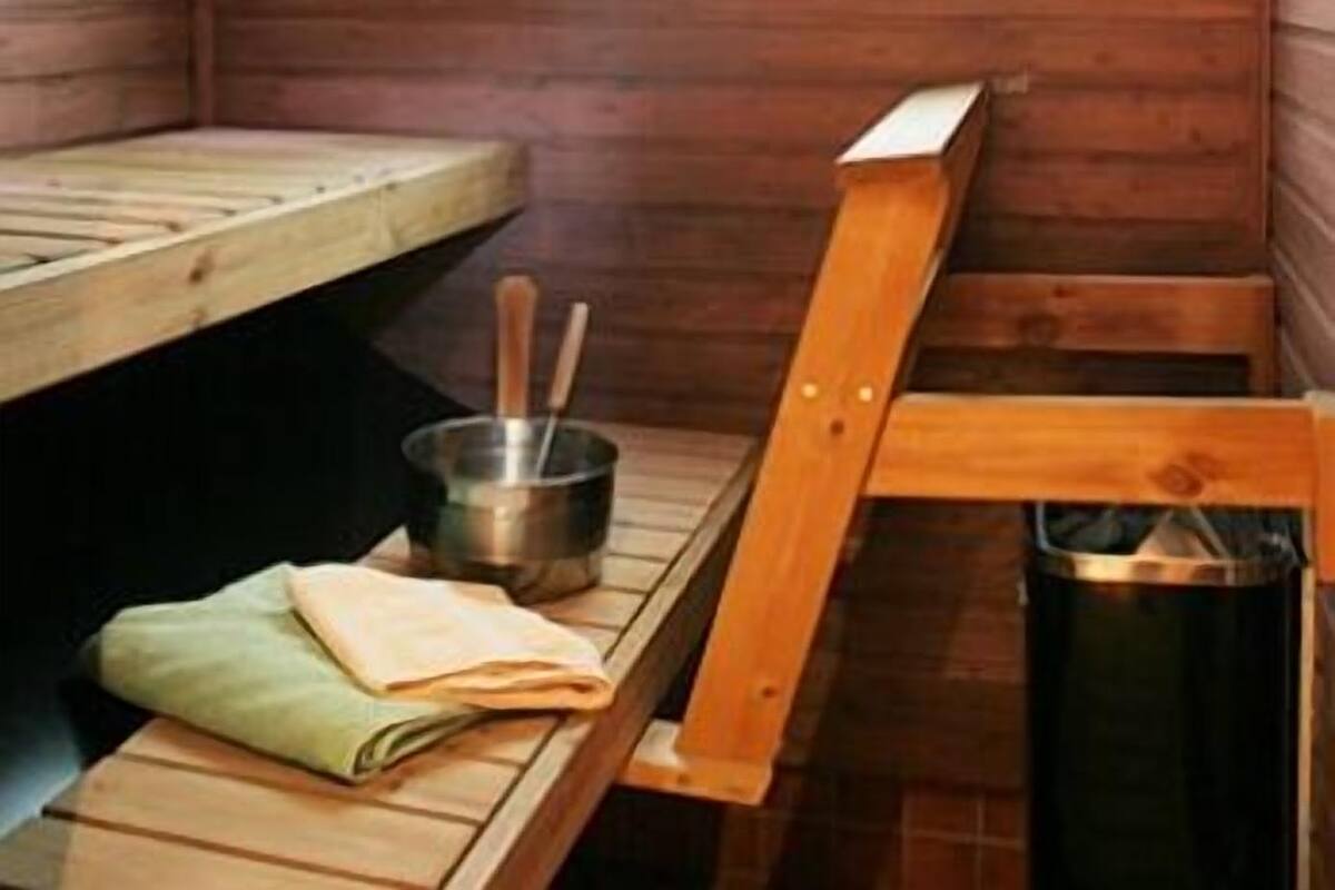 Un cuarto de sauna con bancos de madera, una ventana, un calentador pequeño y un cesto de basura.