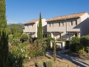 A residential building with a tiled roof, surrounded by greenery and a mountainous backdrop.