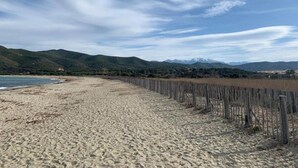 En strand med ett trästaket, en sandstrand och berg i bakgrunden.
