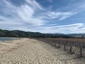 Ein Strand mit einer Holzlattenzaun, sandigem Ufer und Bergen im Hintergrund.