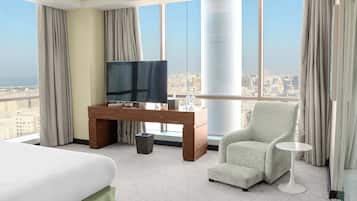 Quarto de hotel com cama, escrivaninha com televisão, cadeira e vista para a cidade.