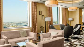 A hotel room with a sofa set, two armchairs, a coffee table, and a view of the cityscape.