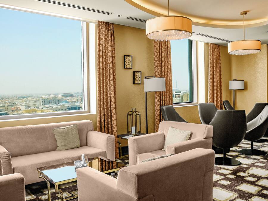 A hotel room with a sofa set, two armchairs, a coffee table, and a view of the cityscape.