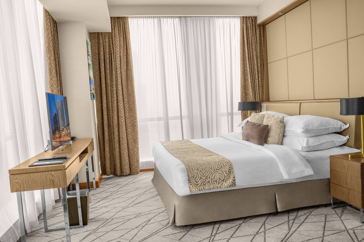 A hotel room with a bed, desk, and curtains.
