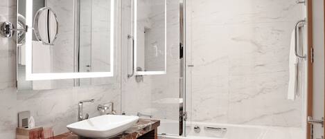 Un baño moderno con lavamanos de mármol, ducha con cerramiento de vidrio y un espejo grande.