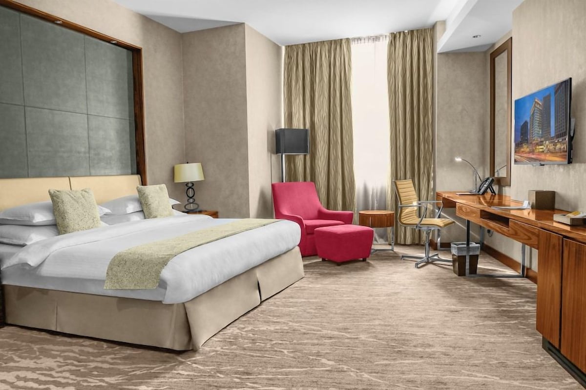 A hotel room with a large bed, a desk, a chair, a lamp, and a television.