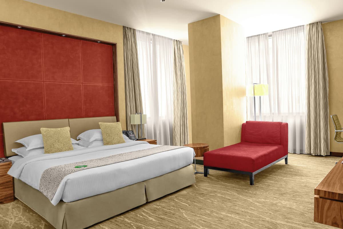 A hotel room with a bed, a red chair, a desk, and curtains.