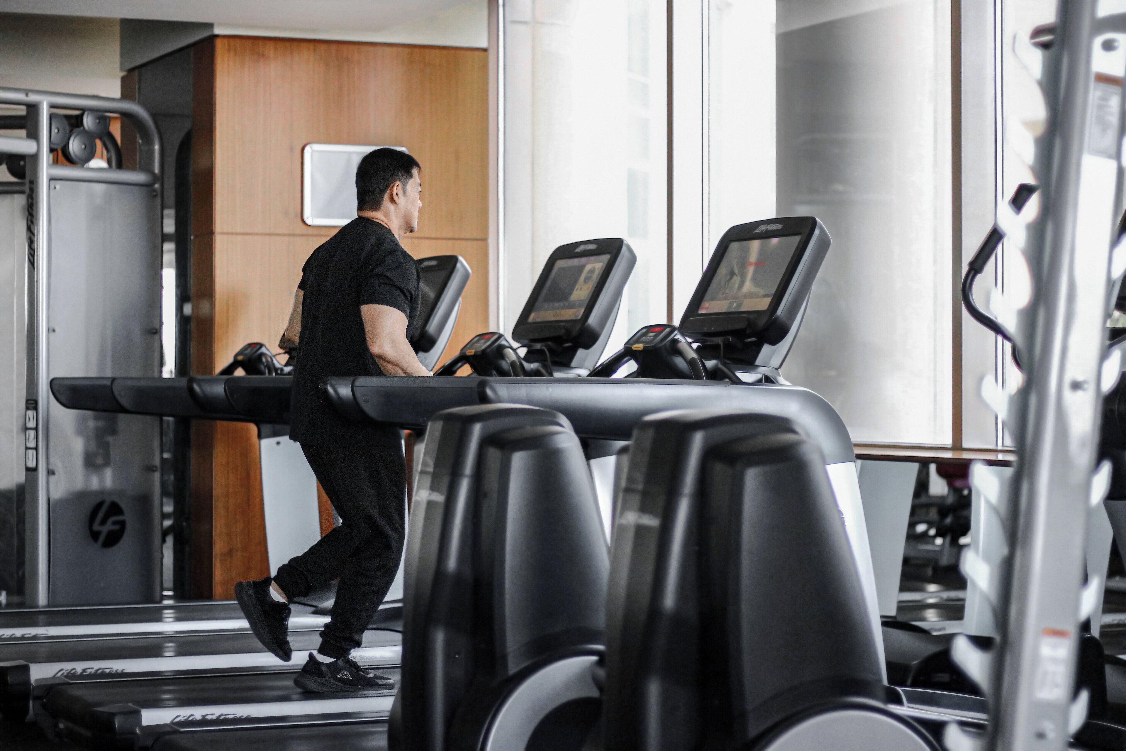 A gym with treadmills, weight machines, and a wooden wall.