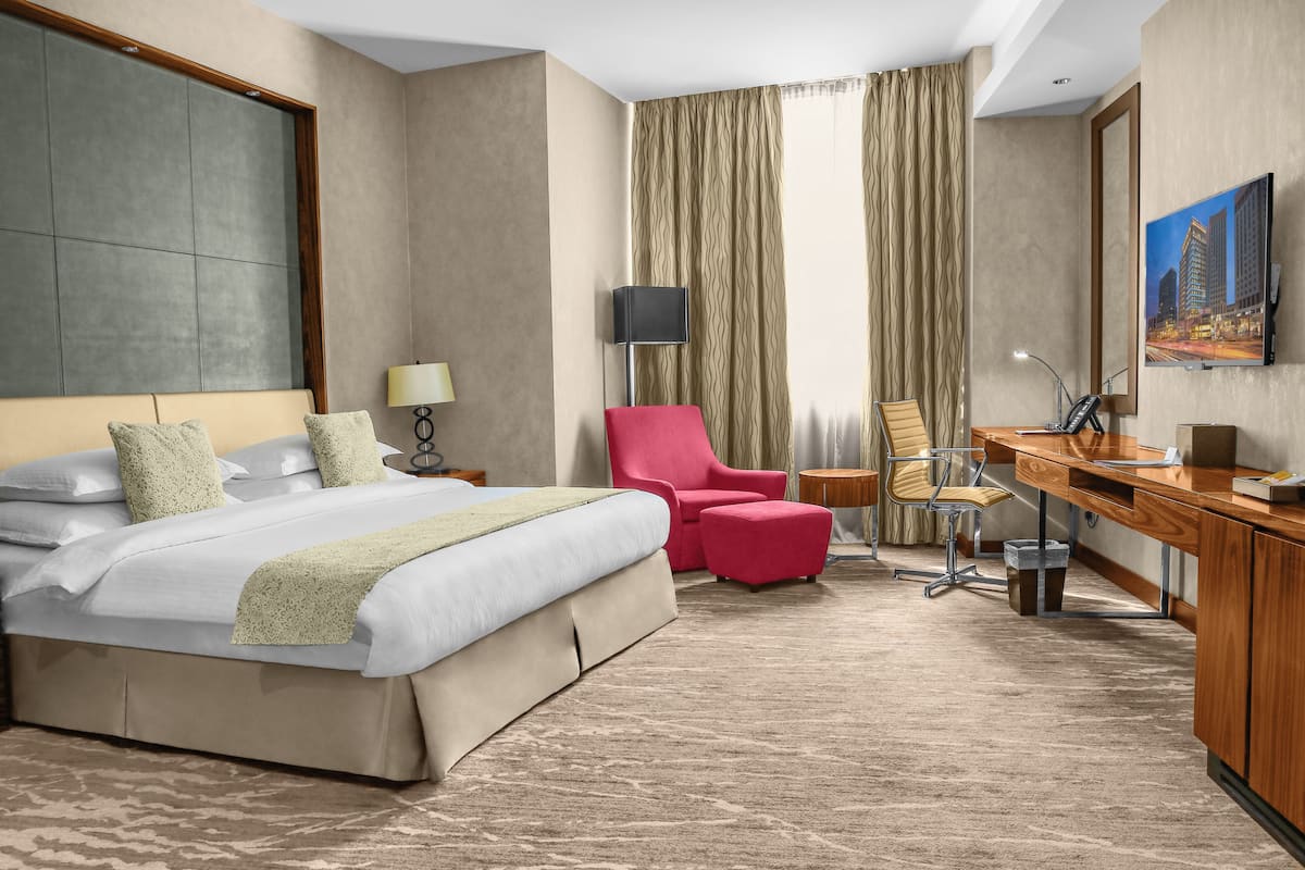 A hotel room with a large bed, a desk, a chair, a lamp, and a painting on the wall.