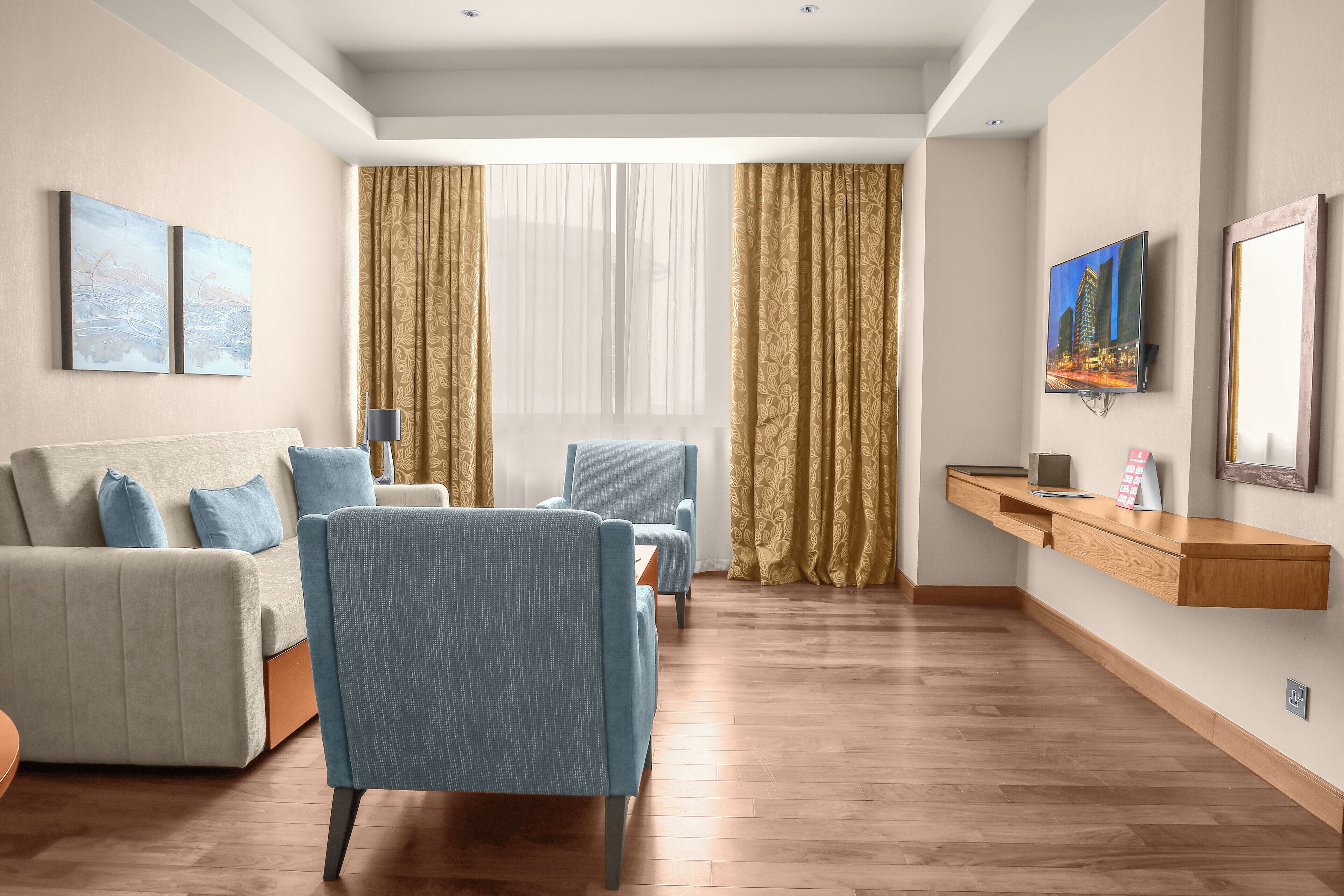 A modern living room with a sofa, armchairs, a TV, and a wooden floor.