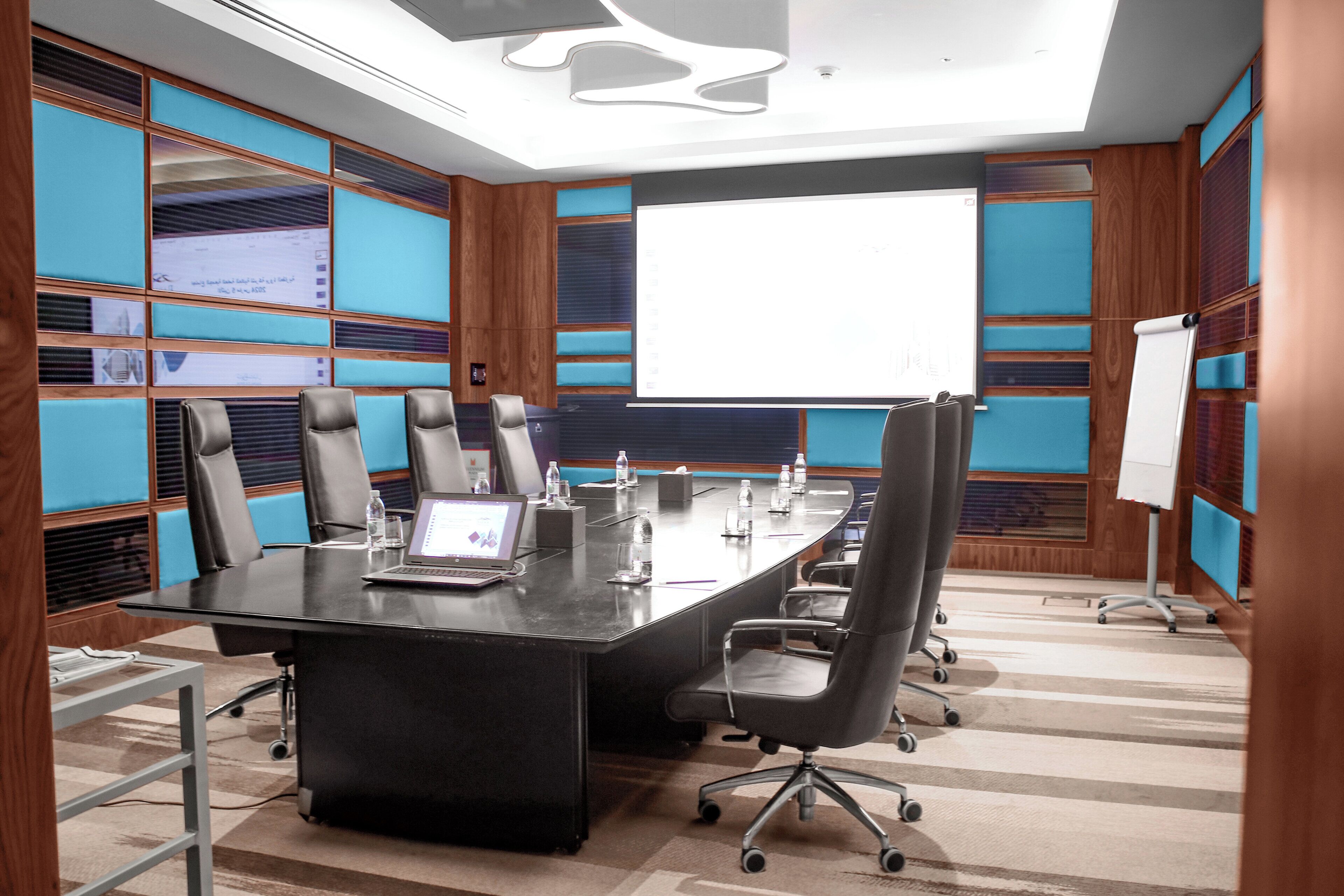 Une salle de conférence avec une longue table, de nombreuses chaises, un ordinateur portable et un écran de projection.