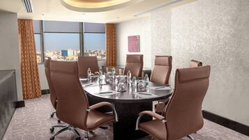 A conference room with a round table, six chairs, and a city view through large windows.