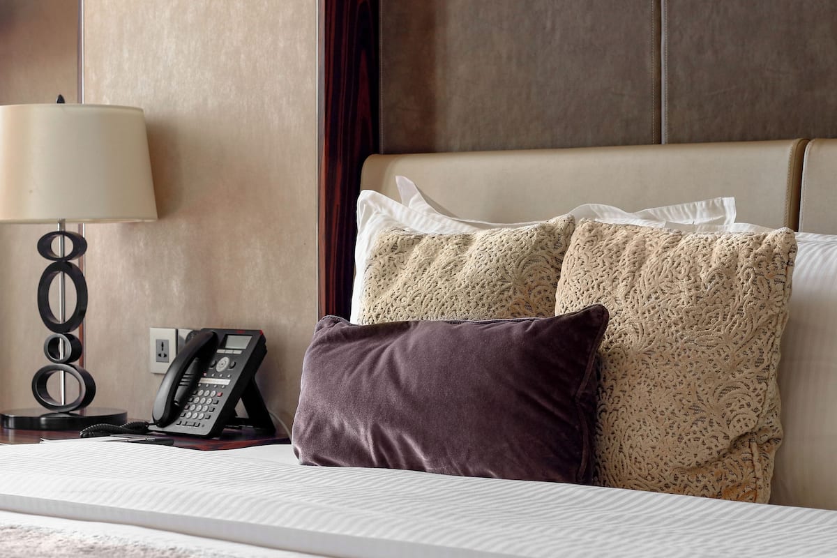 A hotel room with a bed, a telephone, a lamp, and a red chair.