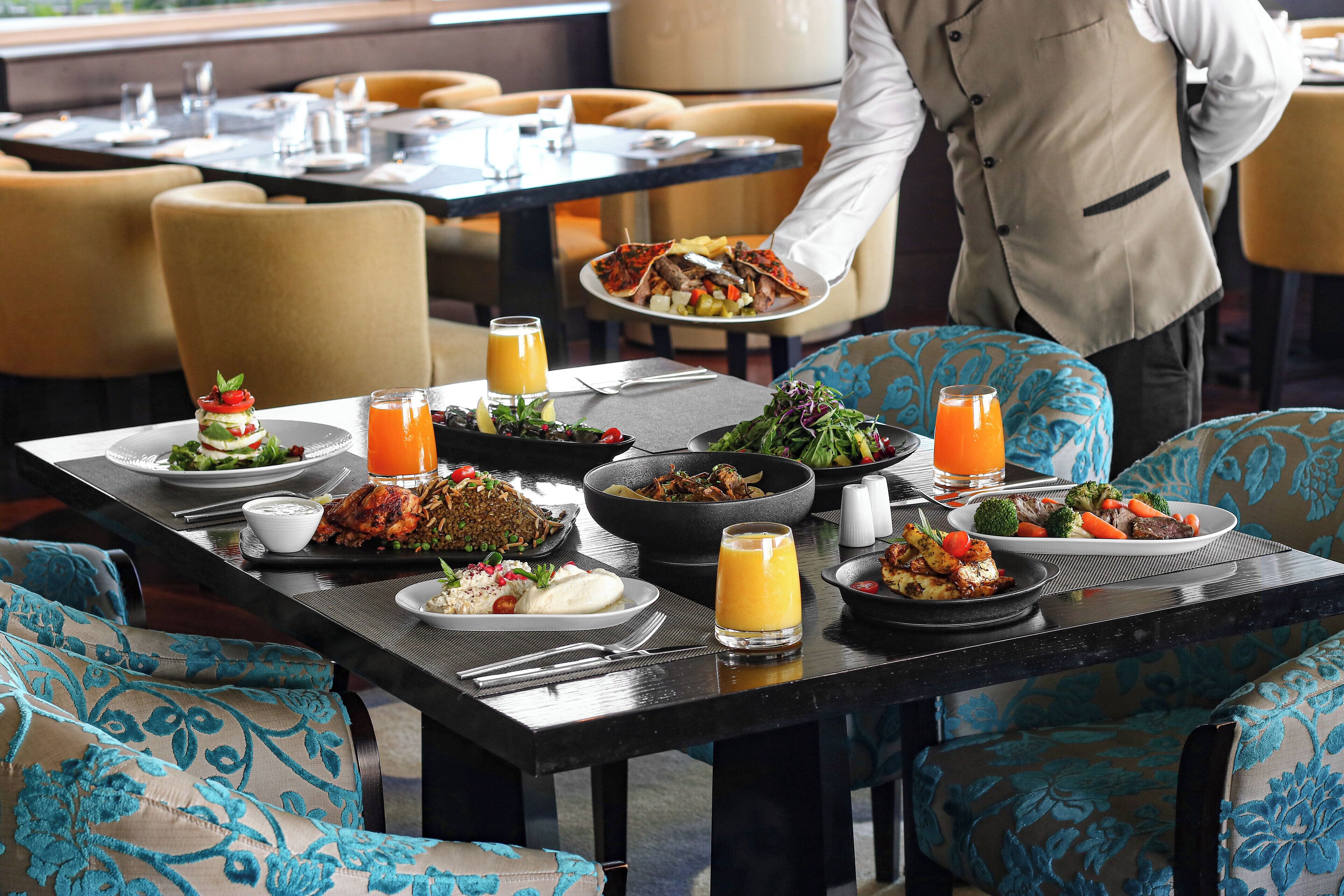 A dining table set with various dishes, a waiter serving food, and a view of the restaurant's interior.