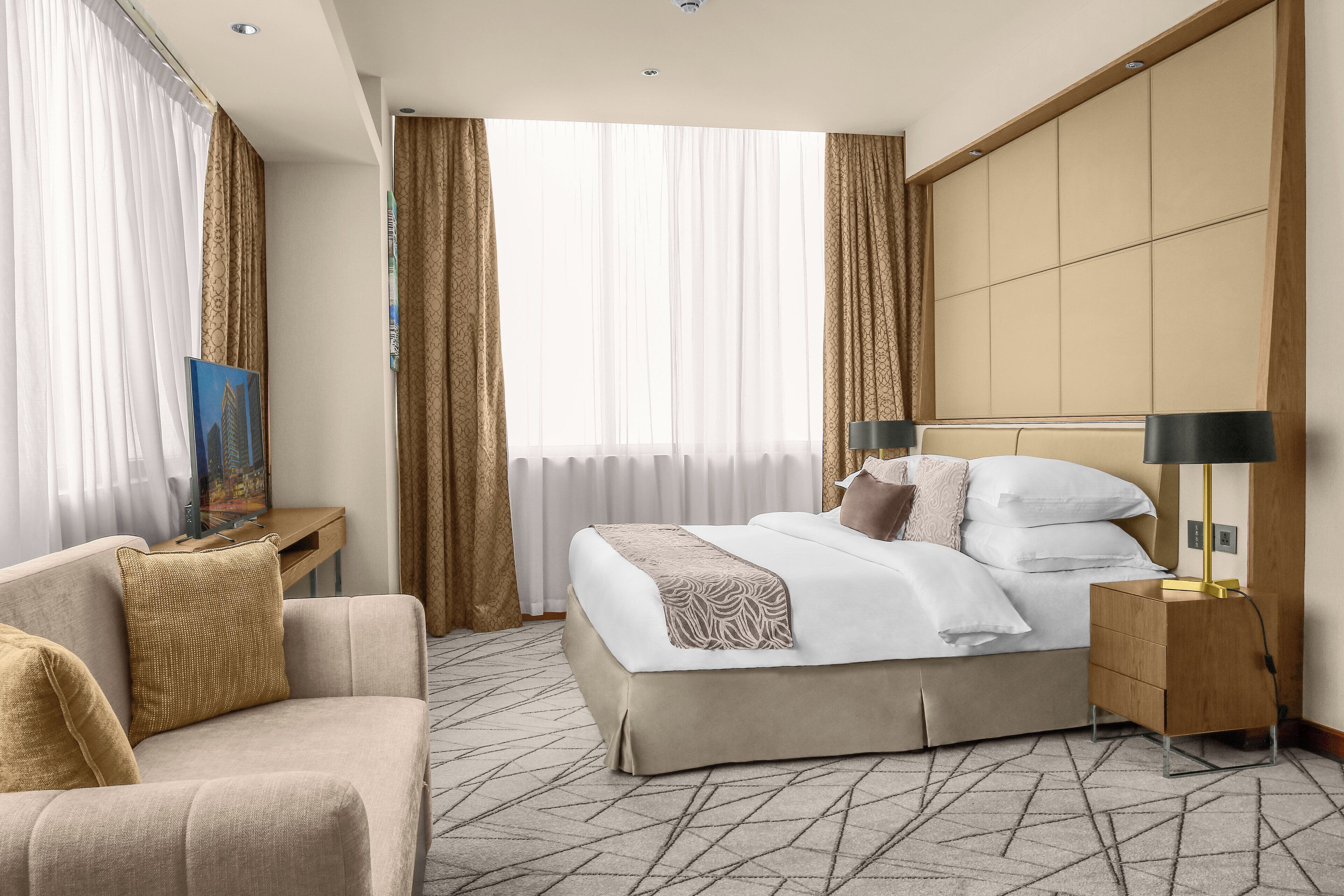 A hotel room with a bed, a sofa, a nightstand, and a large window with curtains.