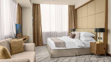 A hotel room with a bed, a sofa, a nightstand, and a large window with curtains.