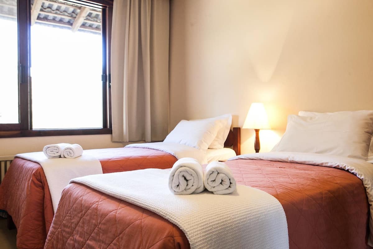Habitación de hotel con dos camas, cada una con una toalla enrollada y ropa de cama blanca.
