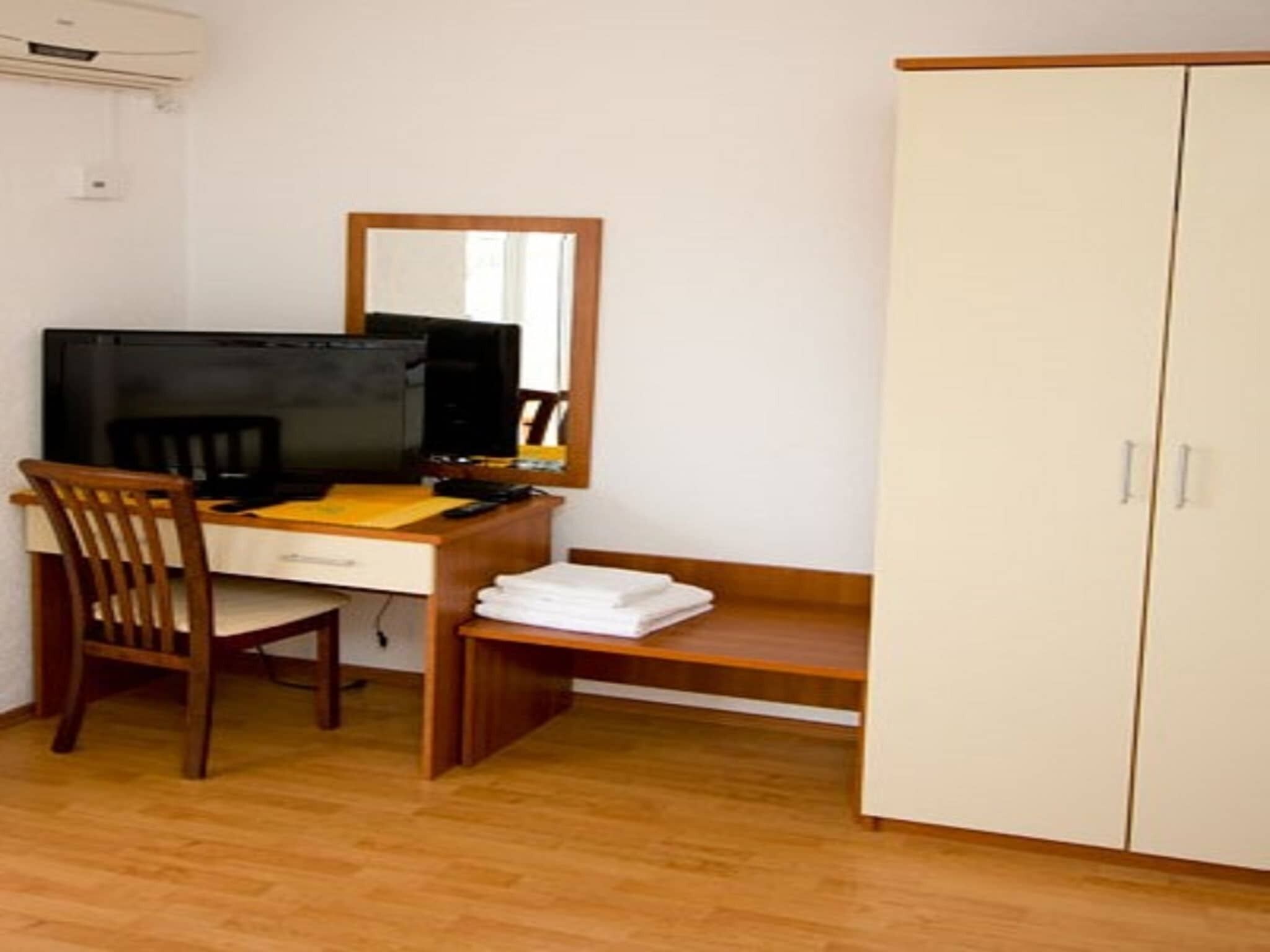 Ein Zimmer mit einem Holztisch, einem Sessel, einem Fernseher, einem Spiegel und einem Kleiderschrank.