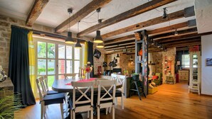 A rustic dining area with a wooden table and chairs, exposed beams, and a stone wall.