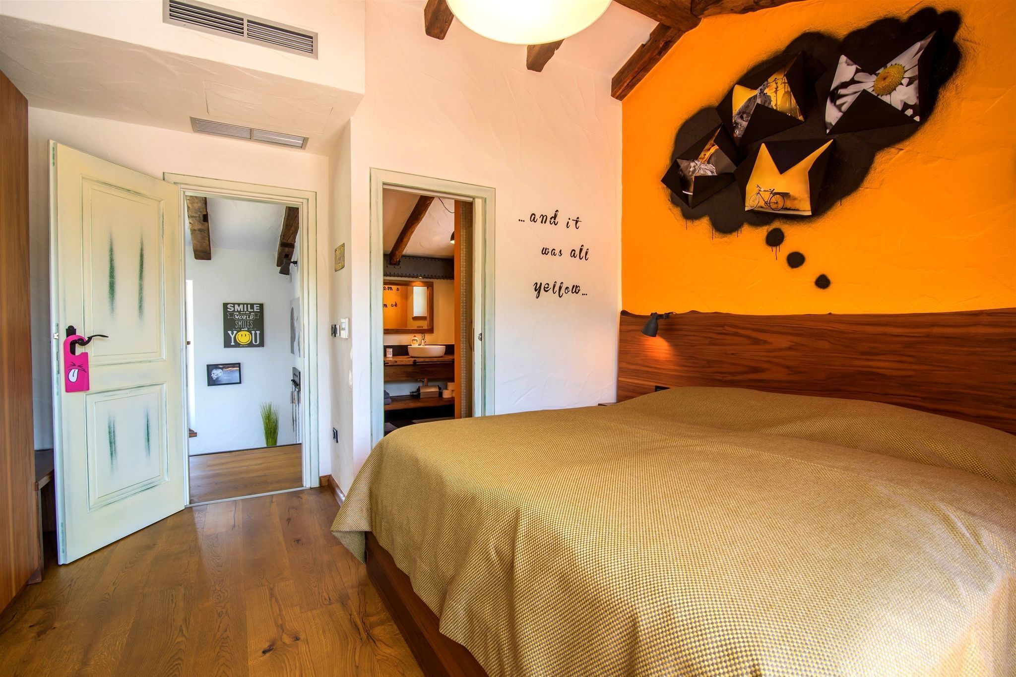 A bedroom with a bed, a wall with a yellow and black abstract design, and a door with a smiley face decoration.