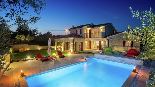 A two-story house with a swimming pool, outdoor seating, and a well-lit patio area.
