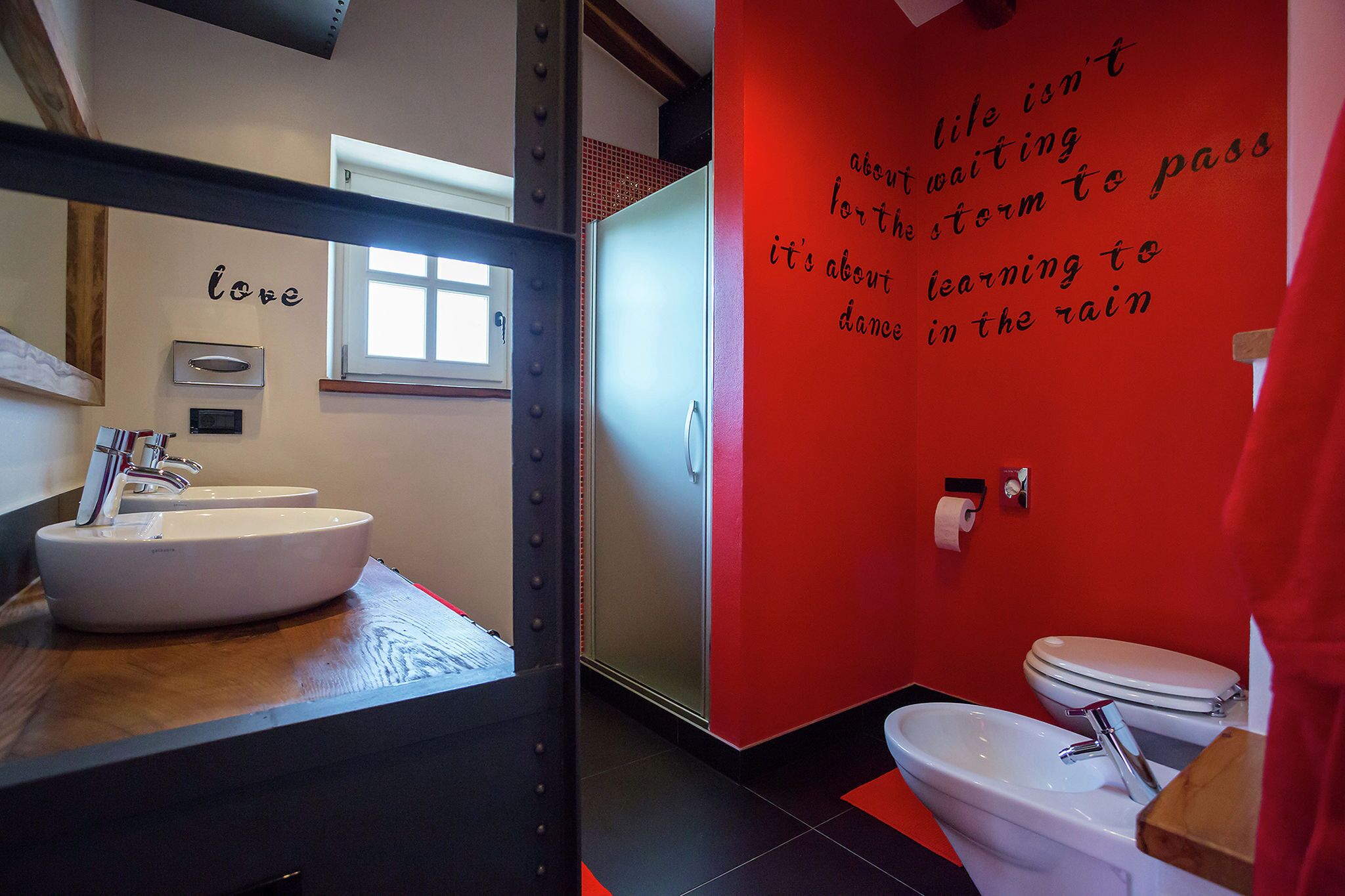 Une salle de bain avec un lavabo blanc, des toilettes et un mur rouge orné d’un texte motivant.