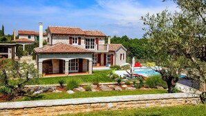 A large stone house with a tiled roof, a swimming pool, and a well-maintained garden.