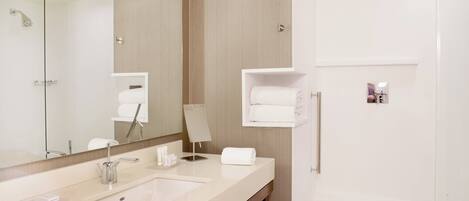 A modern bathroom with a large mirror, two sinks, a shower, and a towel rack.