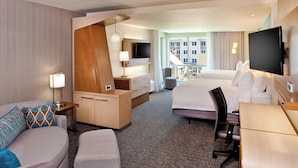 A hotel room with a bed, a desk, a chair, a TV, and a window with a view of buildings.