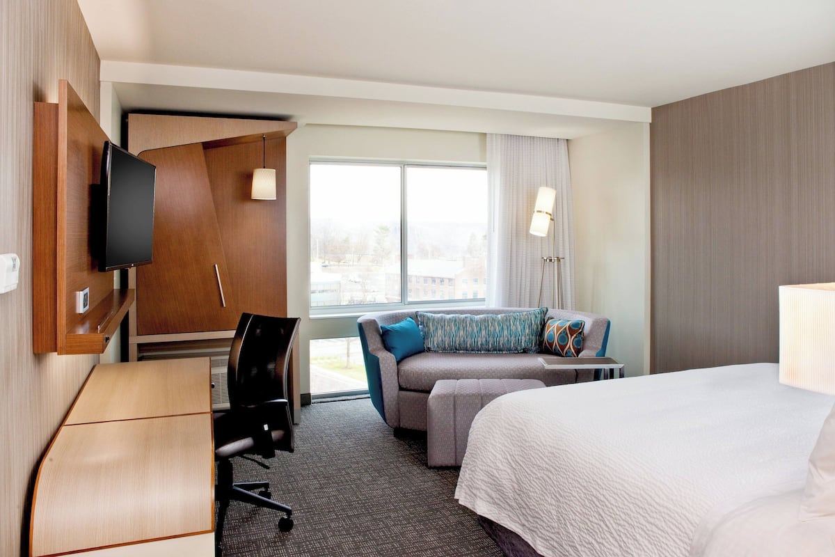 Quarto de hotel com cama, escrivaninha, sofá e televisão.