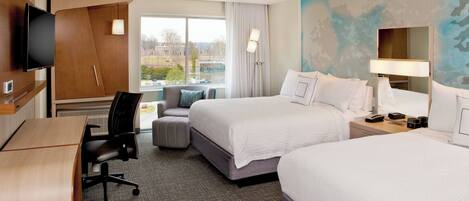 A hotel room with two beds, a desk, a chair, a TV, and a window with a view of buildings.