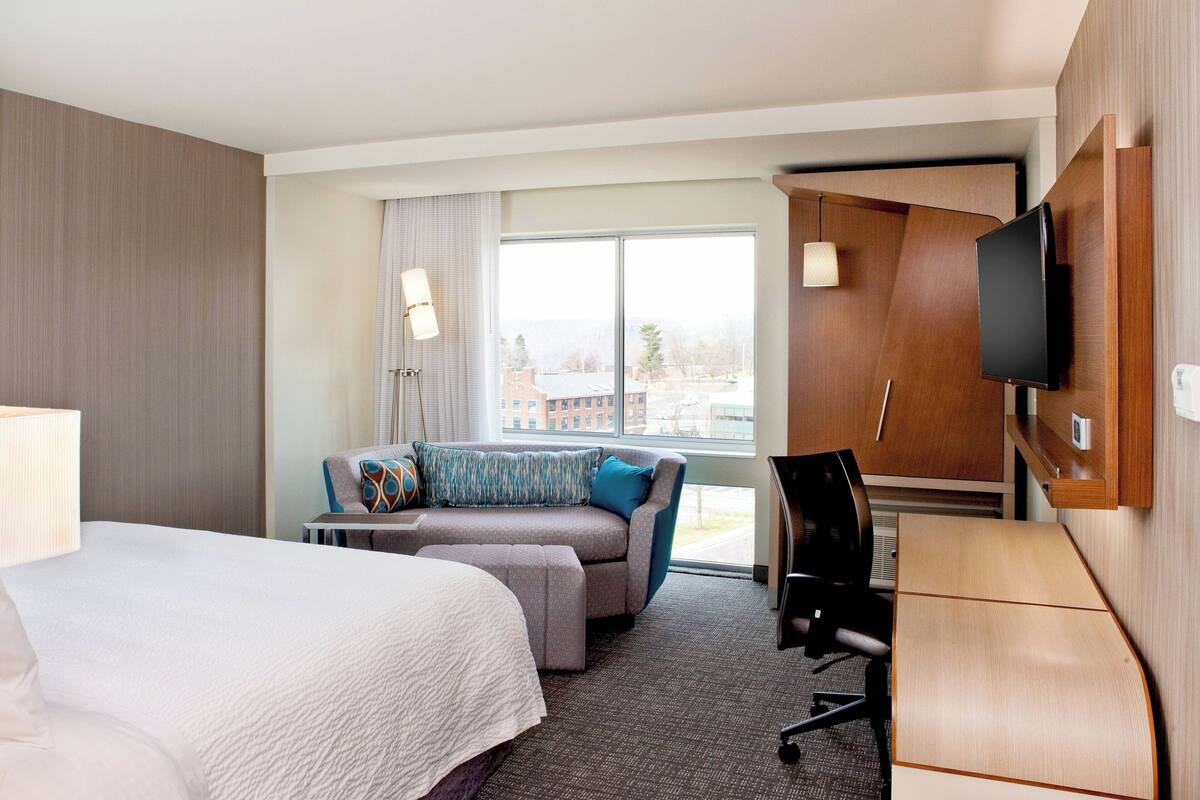 Quarto de hotel com cama, sofá, escrivaninha e televisão.