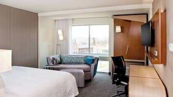A hotel room with a bed, a sofa, a desk, and a TV.