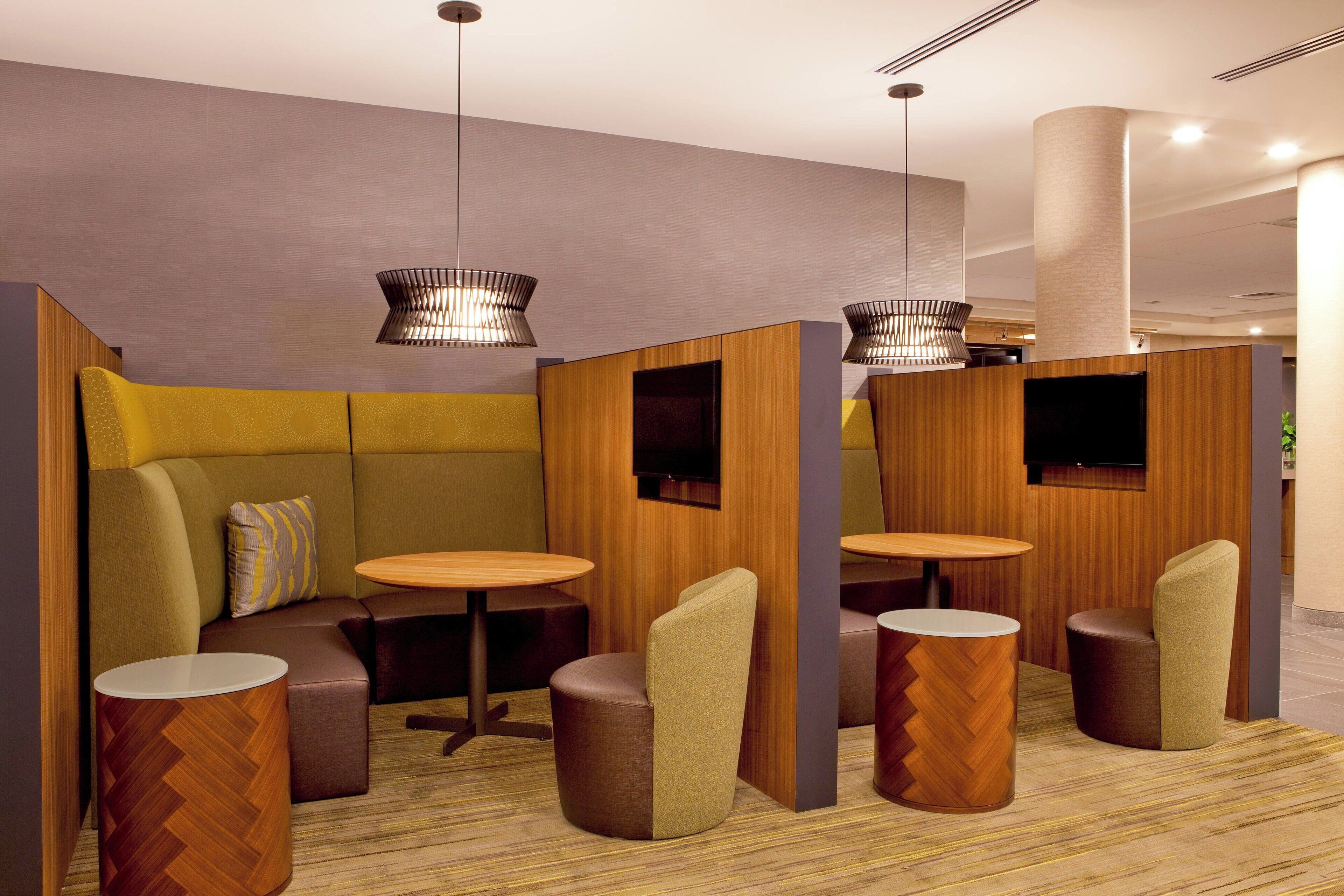 A modern hotel lobby with a seating area featuring cushioned sofas and round tables, wooden accents, and pendant lighting.