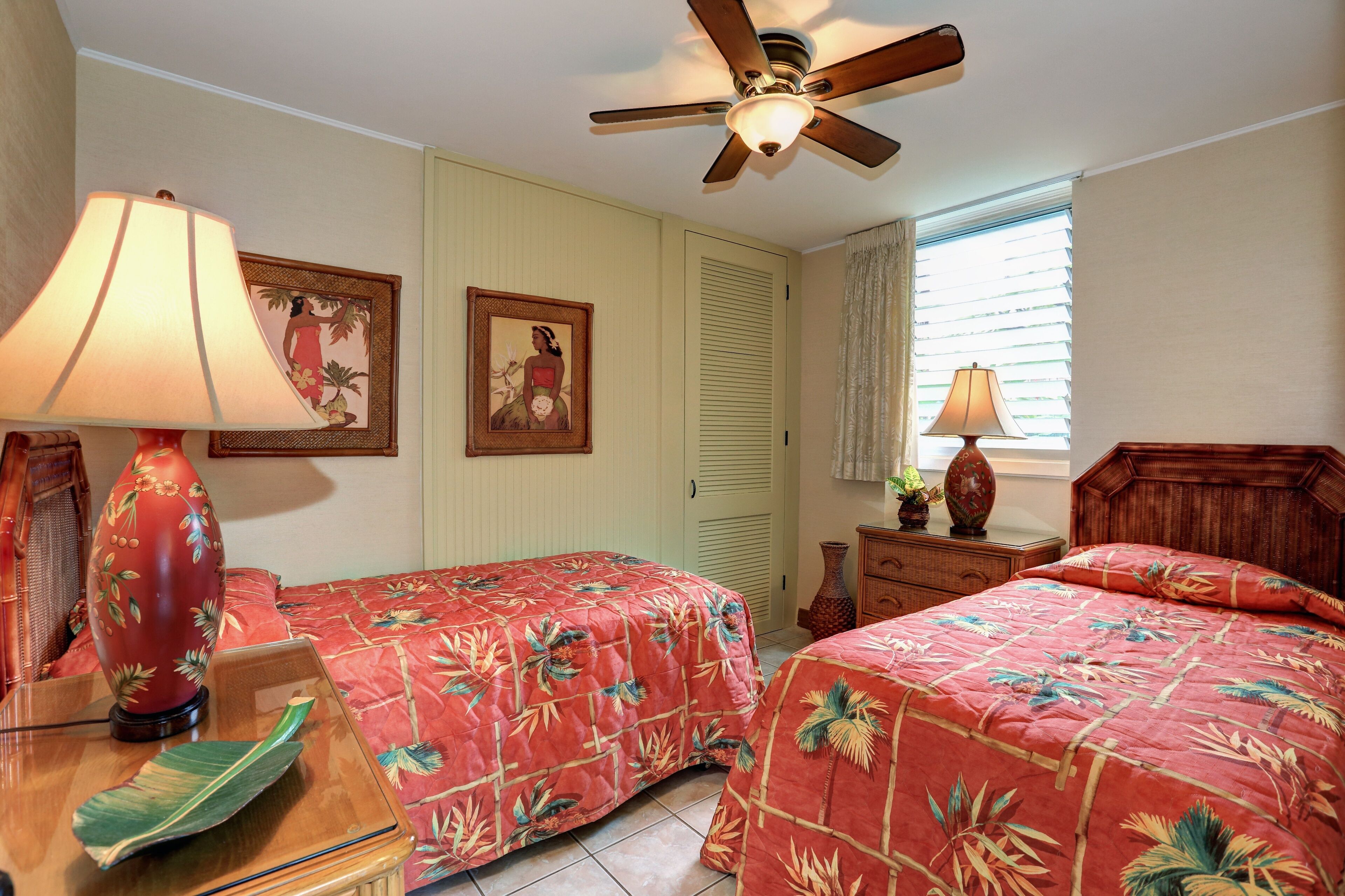 A hotel room with two beds, a ceiling fan, a window with blinds, and a wooden nightstand.
