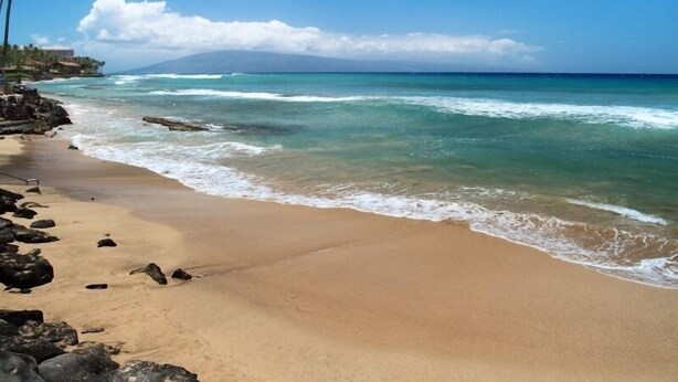 A beach with clear turquoise water, a sandy shore, and a mountain in the background. - Pikake #a6 2 Bedroom Condo by RedAwning (Lahaina)